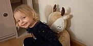 Calista participe au concours pour gagner de l'argent avec cette photo : blonde_hair, cabinet, candid, child, corner, cozy, furniture, indoor, pajamas, plush_toy, portrait, reindeer, shelf, slippers, smile, stuffed_animal, toddler, toy_face, wall, wooden_floor