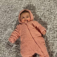 Jordyn is registered to the contest to win money with this photo: baby, infant, pink_onesie, cozy, carpet, floor, indoor, child, smiling, cute, warm_clothing, footwear, lying_down, portrait, soft_texture, hooded, happy, person, small, toddler