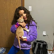 Scout joined the competition — help win amazing prizes! backpack, bedroom, blue_pants, cat, child, curly_hair, electrical_outlet, girl, hugging, indoor, kitten, mirror, orange_cat, person, pet, portrait, purple_jacket, smiling, string_lights, wooden_door