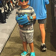 Micah joined the competition — help win amazing prizes! child, boy, sunglasses, baseball_glove, sporting_goods_store, casual_clothing, shorts, tshirt, crocs, carpet, indoor, person, shopping, aisle, footwear, reflection, standing, retail, store, background