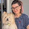 woman, dog, pet, portrait, smile, glasses, braided_hair, pink_hair, striped_shirt, watch, necklace, indoors, chair, long_hair, fluffy_dog, affection, holding, happy, casual, closeup