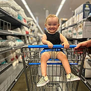 Riley joined the competition — help win amazing prizes! aisle, baby, black_shirt, checkered_shoes, child, clothing, floor, hand, happy, indoor, person, pillows, retail, shelves, shopping, shopping_cart, smiling, store, toddler, walmart