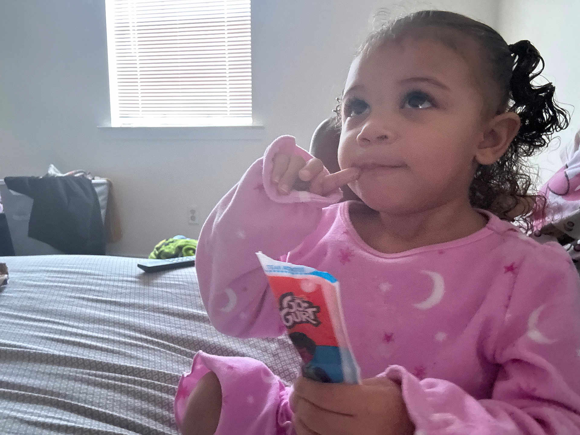 Zhai joined the competition — help win amazing prizes! child, toddler, pajamas, pink_pajamas, snack, bed, window, blinds, remote_control, thoughtful, curly_hair, portrait, indoor, person, food_package, blanket, bedroom, sitting, hand, face