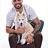 Yuki participe au concours pour gagner de l'argent avec cette photo : armchair, beard, blue_eyes, casual_clothing, dog, furry, hands, happy, husky, indoor, man, pet, portrait, puppy, short_hair, sitting, smile, tattoo, watch, white_background
