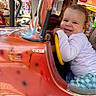toddler, child, smiling, amusement_ride, steering_wheel, curly_hair, colorful, vintage_car, indoor, playful, happy, fun, carnival, seat, vehicle, bright_lights, entertainment, clothing, person, portrait