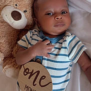 Taige is registered to the contest to win money with this photo: baby, infant, teddy_bear, onesie, striped_clothing, wooden_sign, one_month, bed_sheet, lying_down, hand, face, cute, child, soft_toy, newborn, portrait, sleepwear, resting, indoor, smile