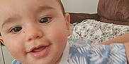 Giuliann a rejoint le concours — aidez-le/la à gagner de superbes lots ! baby, child, close_up, smiling, blue_shirt, patterned_clothing, indoor, living_room, couch, furniture, person, happy, young_child, face, head, curious, sitting, sleeves, home, casual