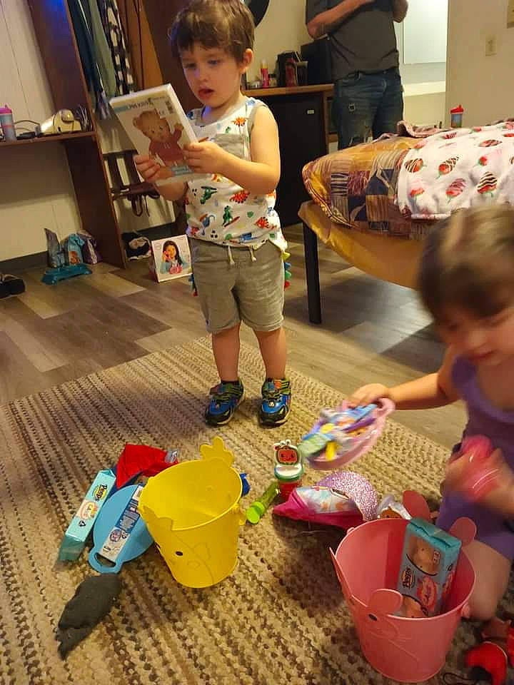 Mason is registered to the contest to win money with this photo: baby, baby_toys, box, child, event, flooring, fun, hardwood, leisure, person, plastic, play, room, sharing, shelf, sitting, toddler, toy, toy_vehicle, visual_arts