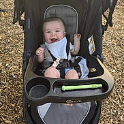 Cole is registered to the contest to win money with this photo: baby, baby_boy, bib, child, clothing, cute, graco, happy, infant, outdoor, person, playground, relaxing, seat, seatbelt, smiling, stroller, sunlight, toy, wood_chips