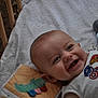 baby, smiling, crib, pillow, toy, pacifier, blanket, face, child, superhero_shirt, happy, infant, crawling_toy, wooden_crib, cute, lying_down, indoor, colorful, playtime, closeup