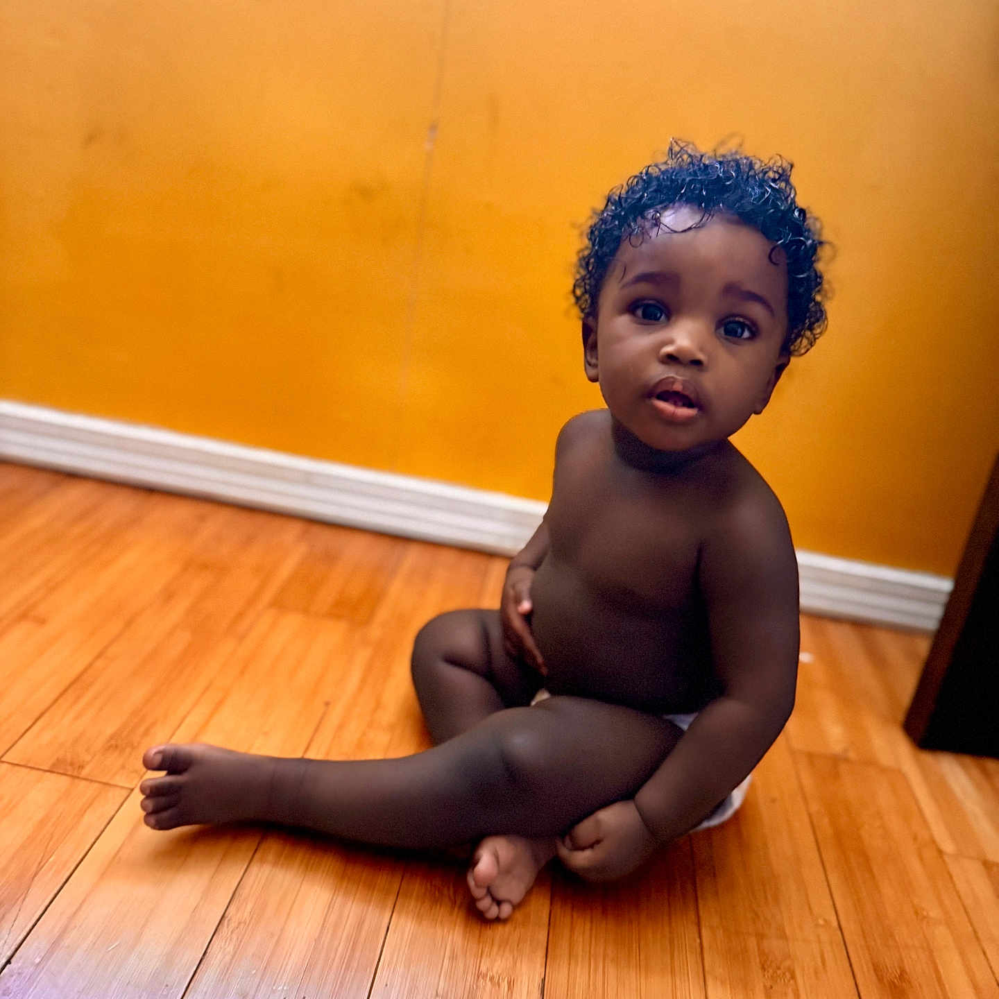 Premier joined the competition — help win amazing prizes! child, toddler, curly_hair, sitting, wooden_floor, orange_wall, indoor, barefoot, diaper, cute, portrait, young_child, skin, baby, expression, looking_up, flooring, home, innocence, casual