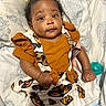 baby, infant, child, orange_clothing, butterfly_pattern, bed, blanket, pillow, cute, fist, lying_down, expression, indoors, soft_toys, pacifier, comfortable, young, person, face, portrait