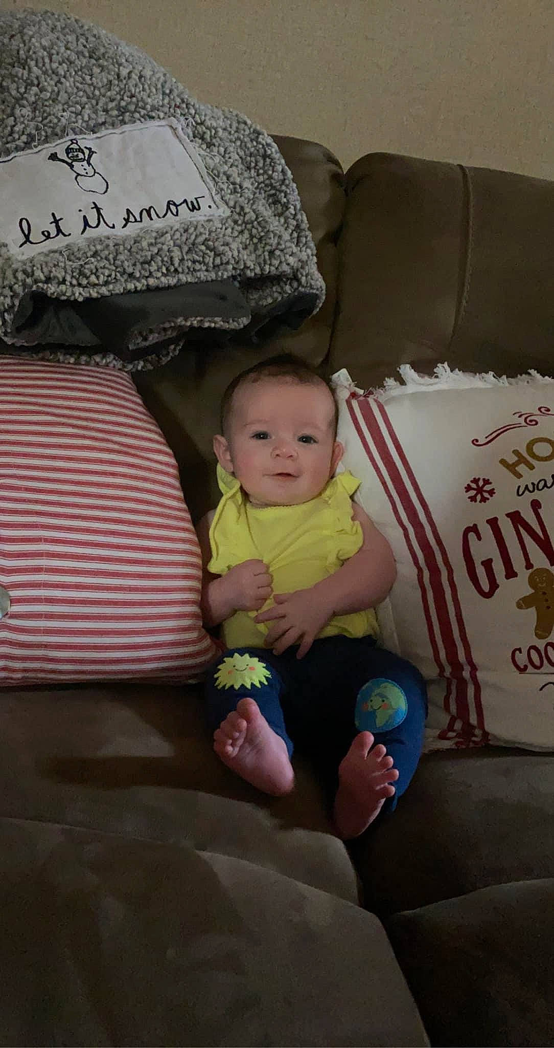 Paisley is registered to the contest to win money with this photo: baby, baby_toddler_clothing, barefoot, cheek, child, comfort, couch, finger, foot, happy, head, lap, linens, person, pillow, product, sitting, textile, thigh, throw_pillow