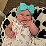 baby, child, headband, bow, floral_dress, cushion, black_and_white, cheeks, hand, face, indoor, comfort, cute, infant, pattern, textile, relaxation, portrait, young, smile