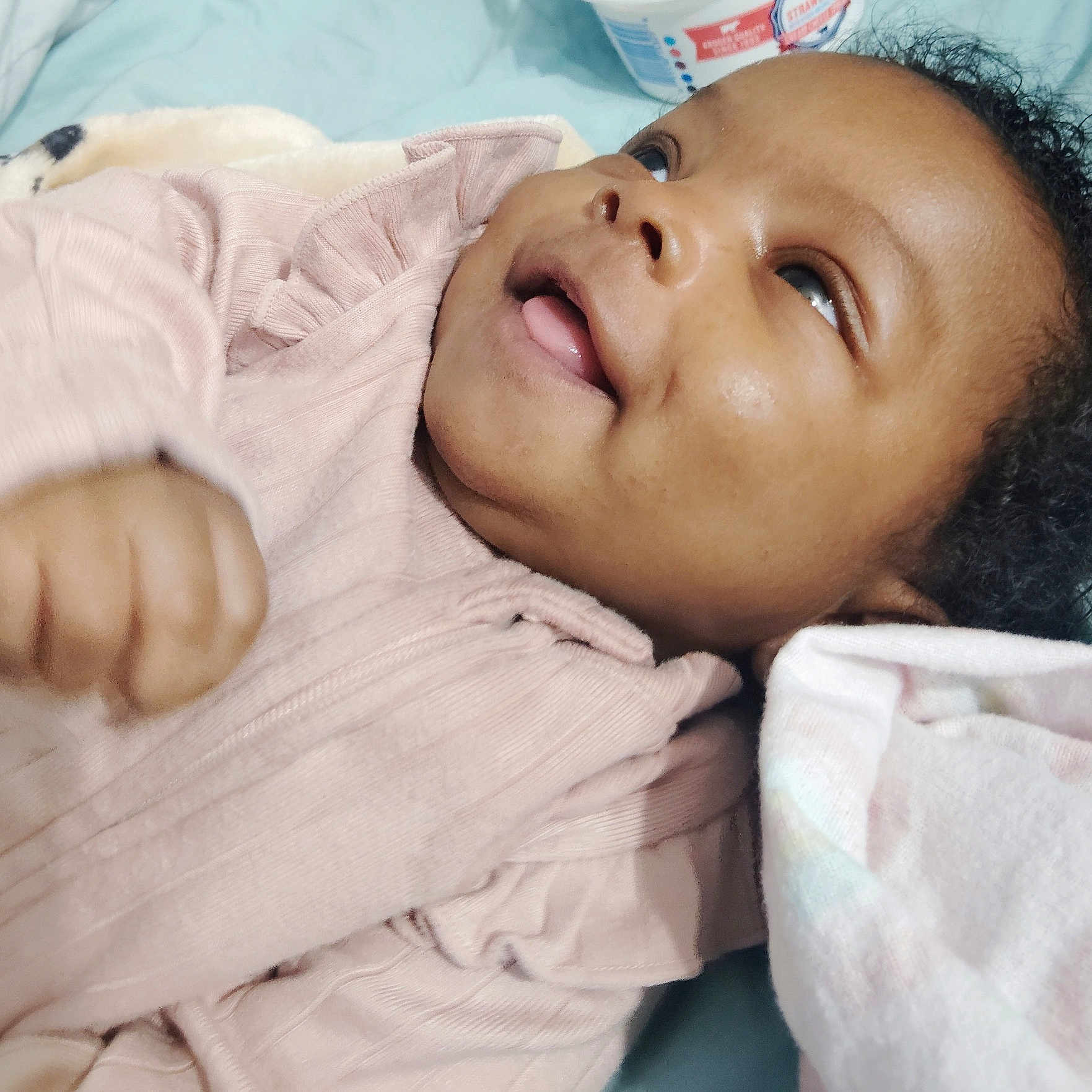 Ember joined the competition — help win amazing prizes! baby, bed, blanket, cheek, child, closeup, cozy, curly_hair, cute, eyes, face, hand, happy, infant, lying_down, pink_clothing, portrait, skin, smiling, tongue