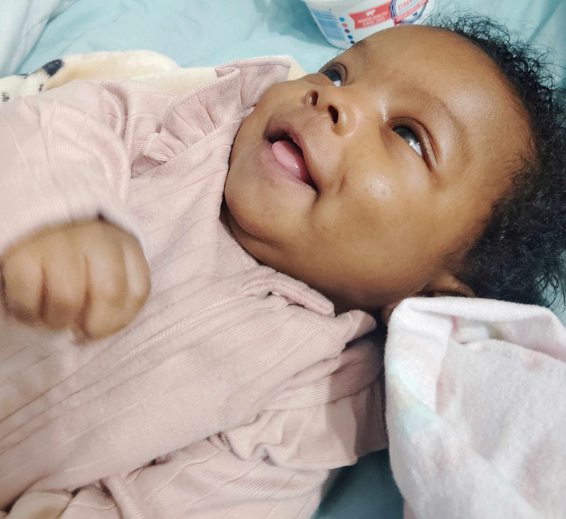 Ember joined the competition — help win amazing prizes! baby, infant, child, smiling, portrait, face, closeup, curly_hair, pink_clothing, blanket, lying_down, hand, eyes, tongue, cheek, skin, happy, bed, cute, cozy