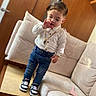 Kaïs a rejoint le concours — aidez-le/la à gagner de superbes lots ! toddler, child, indoor, standing, white_shirt, blue_jeans, sneakers, gold_chain, furniture, couch, wooden_door, floor, curious, person, young_child, casual_clothing, living_room, portrait, cute, home