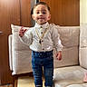 toddler, child, standing, indoor, white_shirt, blue_jeans, sneakers, gold_chain, table, couch, wooden_wall, floor, person, fashion, portrait, casual, cute, smile, hairstyle, accessory