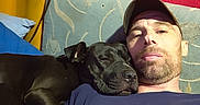 Lotus joined the competition — help win amazing prizes! man, dog, black_dog, couch, red_wall, shoe, cap, facial_hair, relaxing, indoor, snuggling, blue_shirt, resting, pet, companion, casual, home, comfort, closeup, portrait