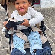 Lyenzo a rejoint le concours — aidez-le/la à gagner de superbes lots ! child, toddler, stroller, curly_hair, smiling, plush_toy, mickey_mouse, pants, shoes, outdoor, cobblestone, seatbelt, happy, person, clothing, footwear, toy, casual_wear, daylight, baby