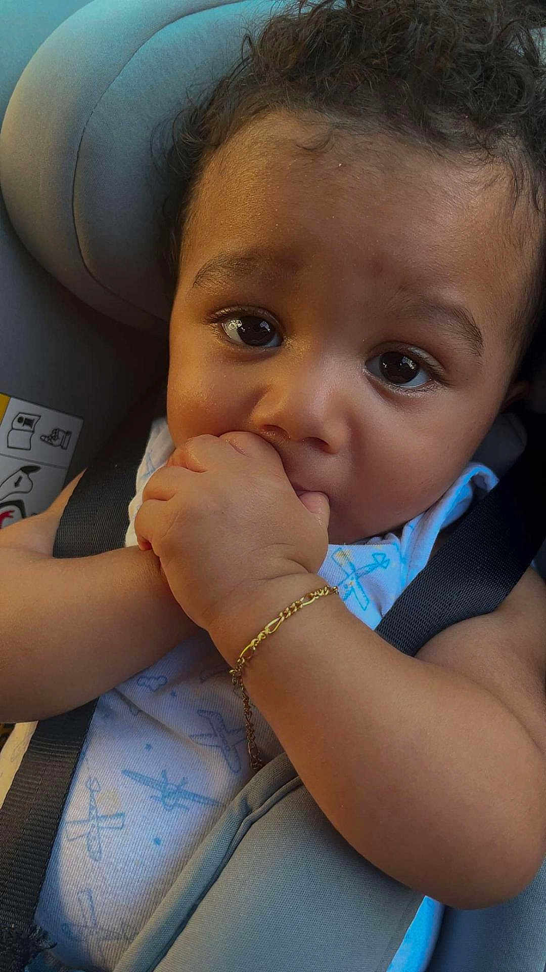 Isaac a rejoint le concours — aidez-le/la à gagner de superbes lots ! baby, child, car_seat, hand_in_mouth, bracelet, curly_hair, close_up, infant, cute, portrait, seatbelt, blue_outfit, airplane_pattern, skin, young_child, looking_at_camera, indoor, soft_lighting, adorable, person