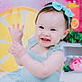 baby, child, smiling, blue_bow, blue_dress, waving_hands, lemon_slice, pink_background, plant, flower, cute, indoors, portrait, happy, sitting, headband, colorful, decor, cheerful, playful