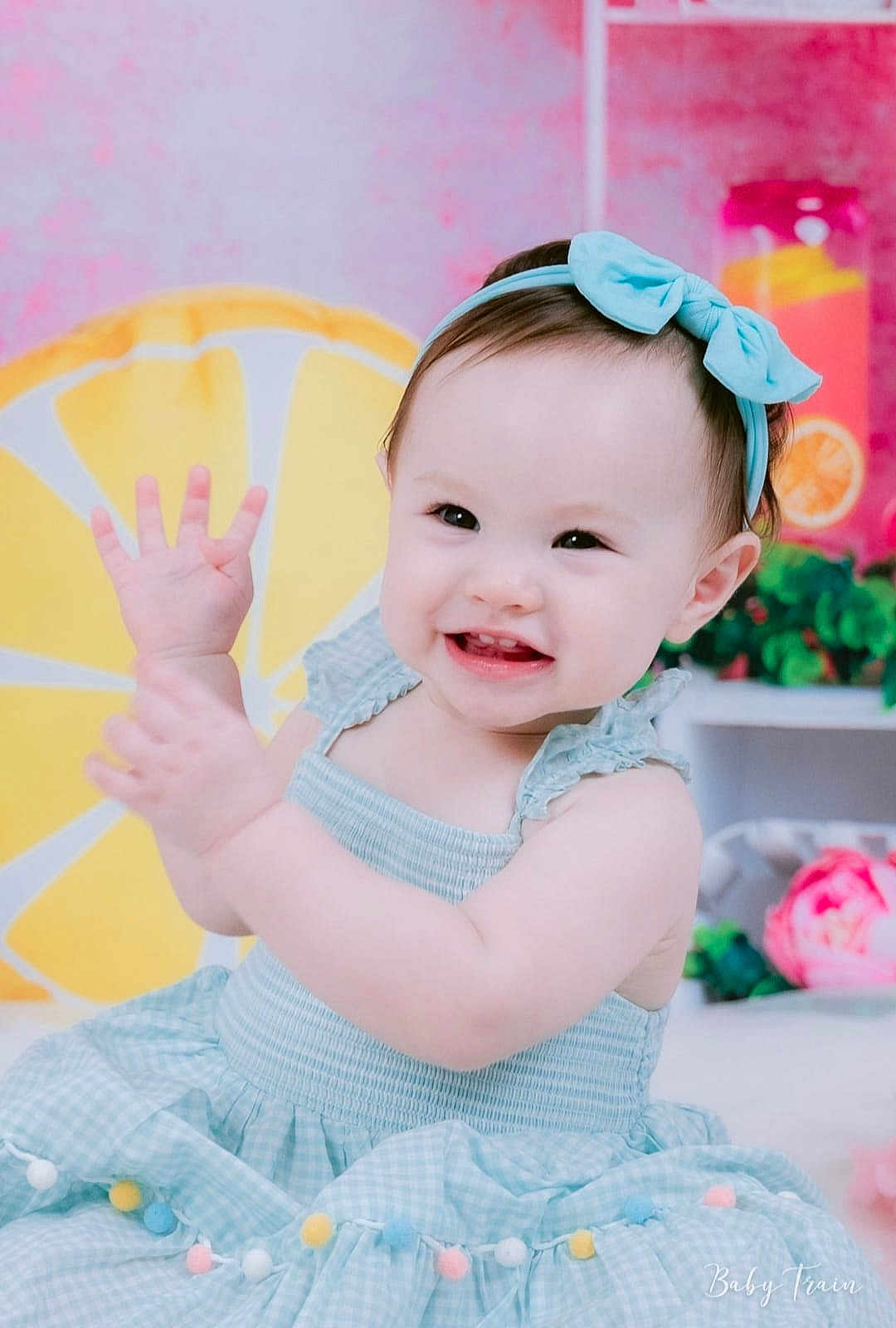 Sophia joined the competition — help win amazing prizes! baby, child, smiling, blue_bow, blue_dress, waving_hands, lemon_slice, pink_background, plant, flower, cute, indoors, portrait, happy, sitting, headband, colorful, decor, cheerful, playful