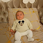 Leao a rejoint le concours — aidez-le/la à gagner de superbes lots ! baby, infant, child, bed, pillow, blanket, mickey_mouse, sweater, booties, portrait, upholstery, headboard, tufted, indoors, cozy, neutral_tones, cute, relaxed, photography, bedding