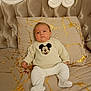 baby, infant, child, bed, pillow, blanket, mickey_mouse, sweater, booties, portrait, upholstery, headboard, tufted, indoors, cozy, neutral_tones, cute, relaxed, photography, bedding