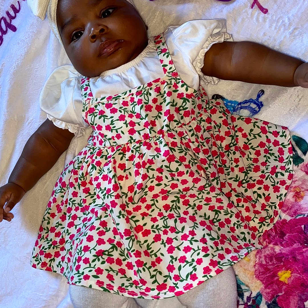 Marielle a rejoint le concours — aidez-le/la à gagner de superbes lots ! arm, baby, blanket, bow, child, colorful, cute, face, floral_dress, flower_pattern, headband, indoors, infant, laying_down, legs, person, portrait, skin, soft_texture, white_tights