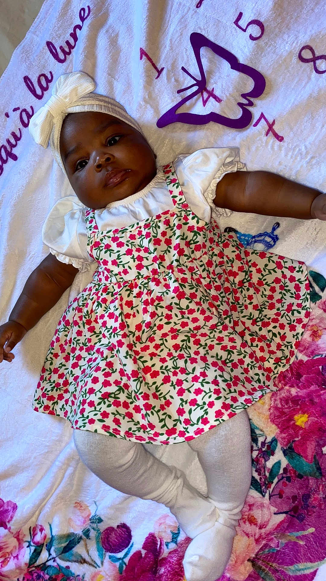 Marielle a rejoint le concours — aidez-le/la à gagner de superbes lots ! baby, infant, child, floral_dress, white_tights, headband, bow, blanket, flower_pattern, laying_down, cute, portrait, indoors, soft_texture, colorful, person, skin, face, legs, arm