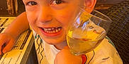 Nëlyo a rejoint le concours — aidez-le/la à gagner de superbes lots ! child, boy, smiling, glass, drink, table, menu, shirt, colorful_clothing, crab_print, duck_print, indoor, warm_lighting, face, happy, sitting, hair, hand, restaurant, wicker_chair