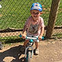 Nëlyo participe au concours pour gagner de l'argent avec cette photo : child, smiling, bike, cap, outdoor, sunlight, fence, grass, footwear, shorts, tshirt, happy, playground, daytime, person, toy, recreation, park, summer, young