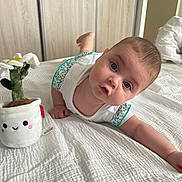 Adèle participe au concours pour gagner de l'argent avec cette photo : baby, infant, bed, white_bedspread, plush_toy, flower_pot, blue_eyes, curious_expression, white_clothing, indoor, wooden_wardrobe, door, child, person, toddler, cute, soft_toy, smiling_toy, home, laying_down