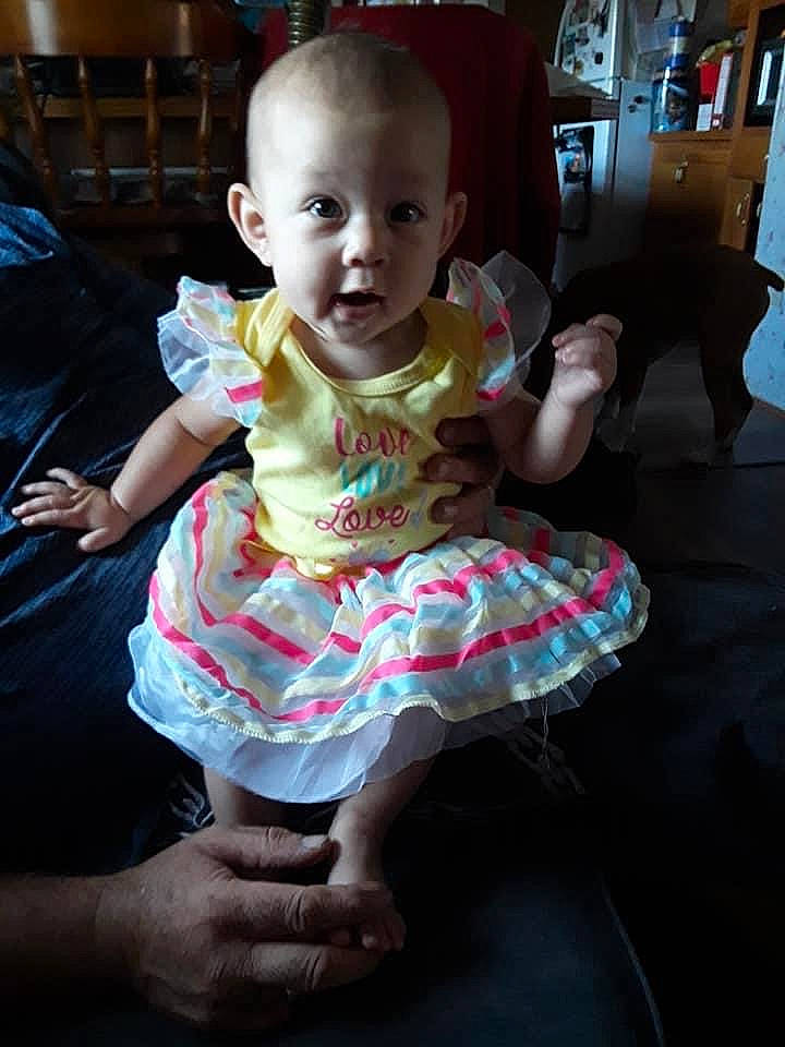 Rhea is registered to the contest to win money with this photo: baby, baby_products, baby_toddler_clothing, child, day_dress, dress, embellishment, finger, floor, foot, hand, living_room, one_piece_garment, person, pink, ruffle, sitting, skin, sock, thumb