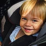 child, toddler, car_seat, blonde_hair, blue_eyes, smiling, sunlight, seatbelt, happy, cute, portrait, baby_clothes, safety, indoors, closeup, young_child, face, person, seat, car_interior