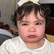 Aisha joined the competition — help win amazing prizes! toddler, child, face, hair_bow, curly_hair, white_shirt, flower_print, hand, container, colorful, hair_ties, indoor, furniture, person, portrait, expression, cute, baby, skin, clothing