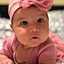 baby, infant, pink_bow, headband, pink_clothing, lying_down, chubby_cheeks, wide_eyes, soft_focus, indoor, cute, child, portrait, close_up, skin, hand, expression, adorable, toddler, face