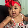 baby, child, red_bow, headband, floral_dress, curious, close_up, indoor, portrait, cute, infant, reaching_out, face, skin, earrings, expression, soft_background, person, young_child, colorful_clothing