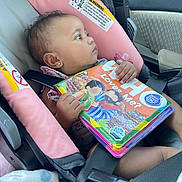 Kaizlee joined the competition — help win amazing prizes! baby, blanket, book, car, car_seat, child, clothing, colorful, cute, holding, infant, interior, pacifier, pink, portrait, reading, safety, seatbelt, side_view, young_child