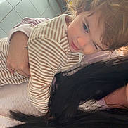 Inaya a rejoint le concours — aidez-le/la à gagner de superbes lots ! adult, chair, child, curtains, face, floor_tiles, hair, hand, holding, home, indoor, long_hair, natural_light, pajamas, person, plant, playful_expression, striped_clothing, toddler, window