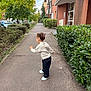 Inaya a rejoint le concours — aidez-le/la à gagner de superbes lots ! apartment, beige_sweater, black_pants, bushes, casual_clothing, child, daylight, greenery, hairstyle, motion, nature, outdoor, pavement, playful, residential_building, sidewalk, toddler, trees, urban, white_shoes