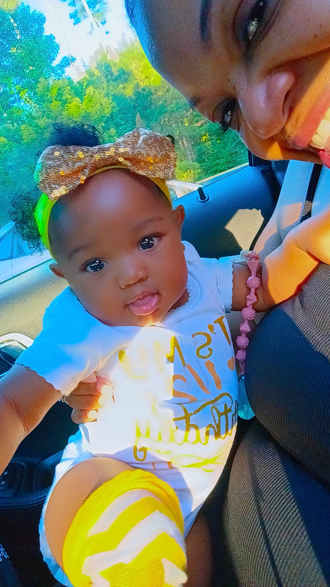 Eliana is registered to the contest to win money with this photo: baby, bow, car_interior, child, clothing, cute, face, greenery, hand, happy, headband, nature_outside, person, portrait, seat, smile, socks, sunlight, window, yellow