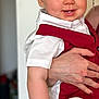 baby, child, person, smile, face, hand, red_clothing, white_clothing, shirt, vest, portrait, indoor, cute, young_child, holding, happy, blue_eyes, short_hair, skin, adult