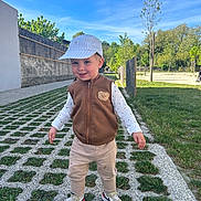 Tiago participe au concours pour gagner de l'argent avec cette photo : cap, casual_clothing, child, daylight, fence, grass, happy, nature, outdoor, pants, park, person, sidewalk, sky, smile, sneakers, toddler, trees, vest, walking
