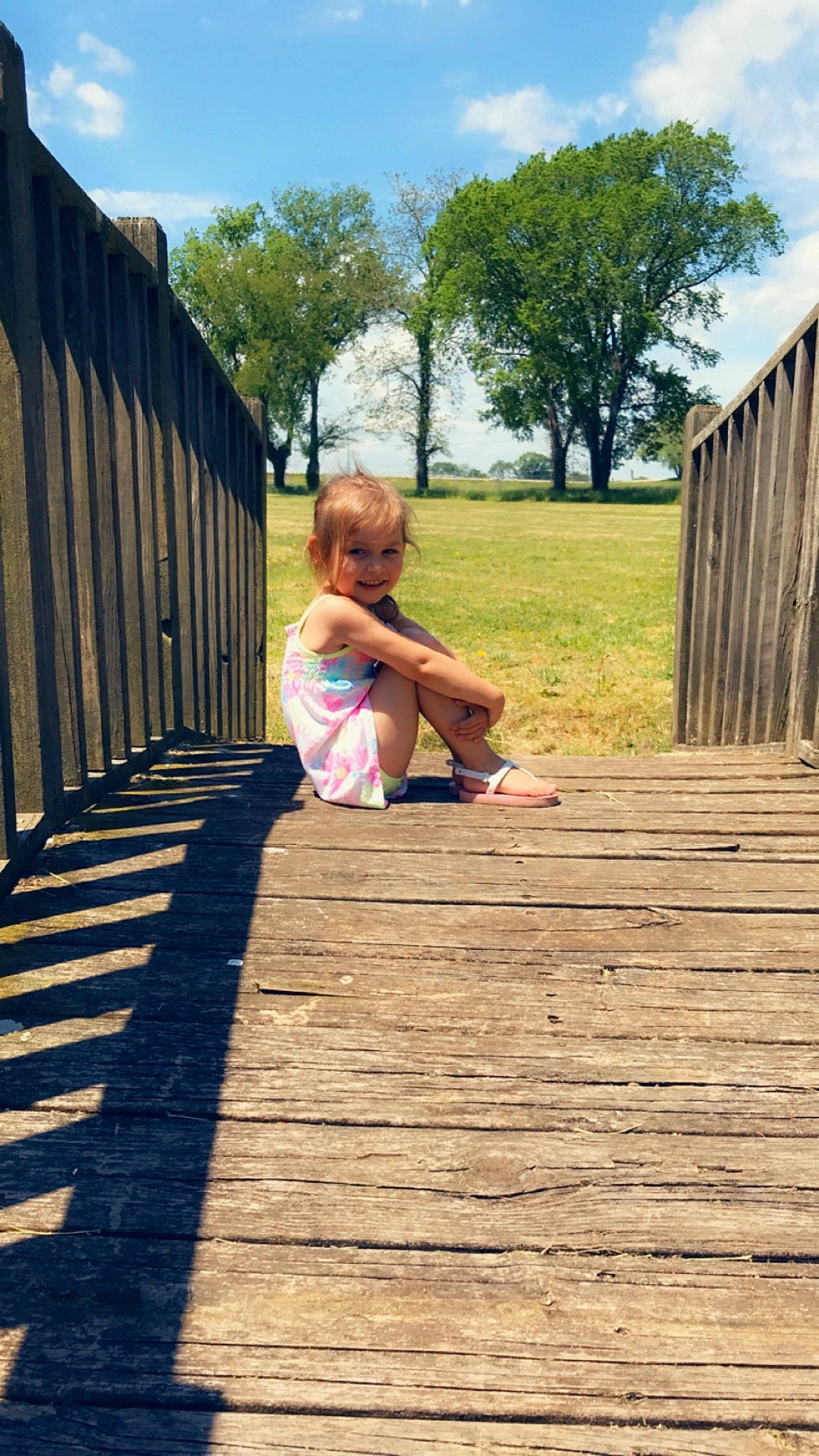 Alyssia is registered to the contest to win money with this photo: boardwalk, child, deck, dock, fence, grass, joy, leg, leisure, outdoor_structure, person, plant, play, shadow, sitting, summer, toddler, tree, vacation, walkway