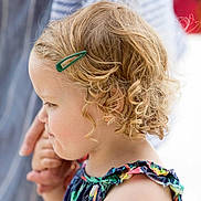 Issy is registered to the contest to win money with this photo: child, toddler, curly_hair, blonde, hair_clip, holding_hands, colorful_dress, floral_pattern, side_profile, portrait, outdoor, adult_hand, close_up, soft_background, cute, young_child, summer_clothing, skin, person, tender_moment