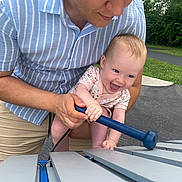 Sophia is registered to the contest to win money with this photo: baby, adult, outdoor, xylophone, music, playing, joyful, smiling, park, greenery, person, child, instrument, summer, fun, happy, holding, pavement, casual_clothing, interaction