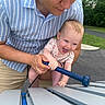 baby, adult, outdoor, xylophone, music, playing, joyful, smiling, park, greenery, person, child, instrument, summer, fun, happy, holding, pavement, casual_clothing, interaction