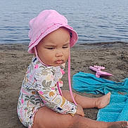 Romy a rejoint le concours — aidez-le/la à gagner de superbes lots ! baby, beach, blue, child, hat, infant, nature, ocean, outdoor, pink, sand, serious, sitting, summer, sunhat, swimsuit, towel, toy, vacation, water